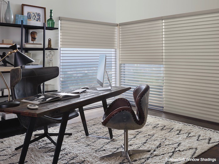 A home office with dark leather chairs and light beige rug and shades.